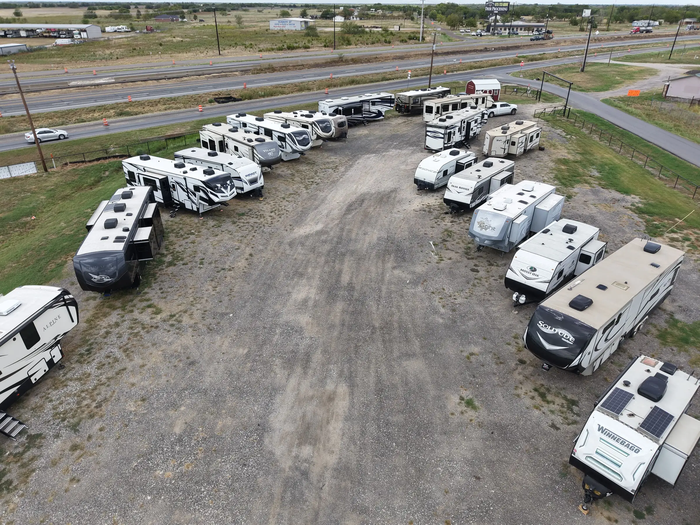 Fifth wheels and travel trailers lining both sides of the center aisle at the BK Consignments lot in Greenville, Texas