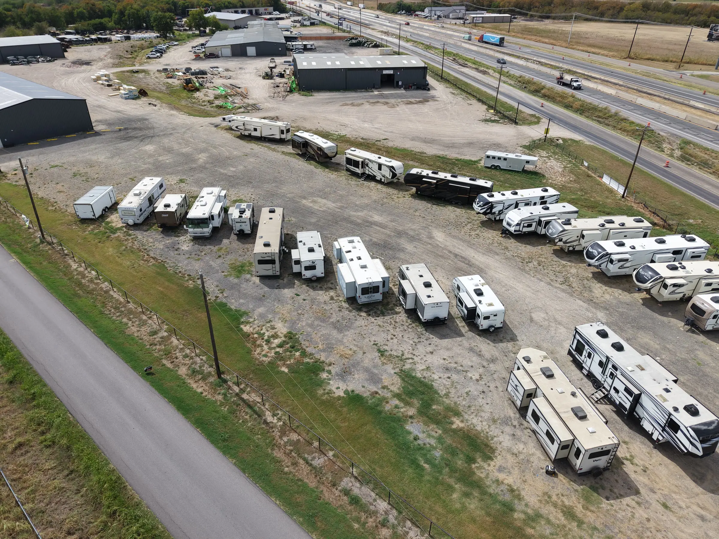 Consigned travel trailers and fifth wheels lined up along Interstate 30 at BK Consignments in Greenville, Texas, seen from a drone