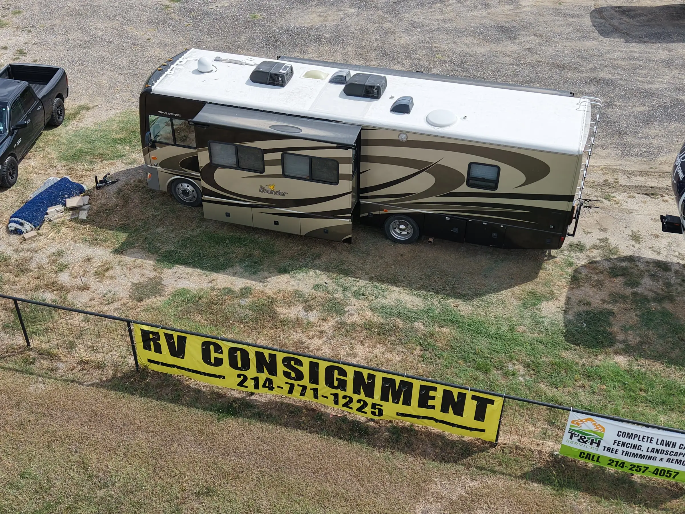 Yellow RV CONSIGNMENT sign with the phone number 214-771-1225 on the fence at BK Consignments in Greenville, Texas